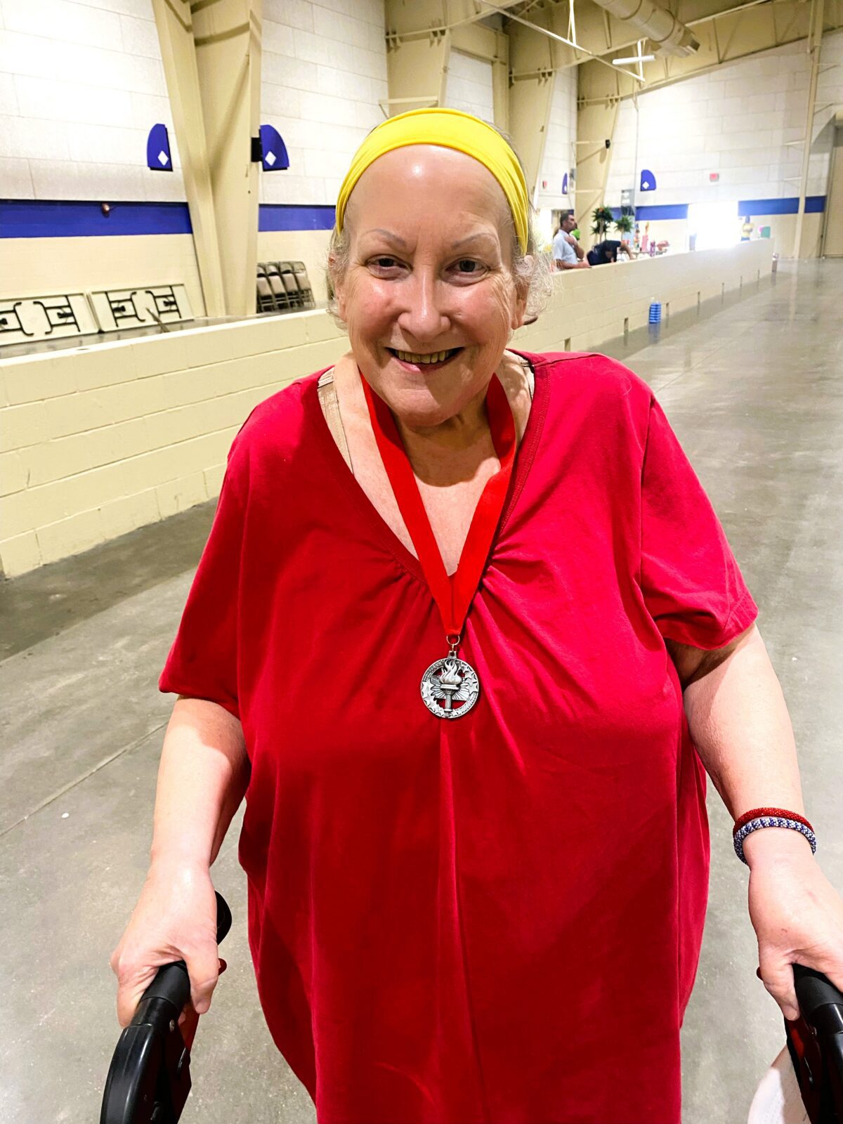 Adult senior female with red shirt, yellow headband and silver medal.